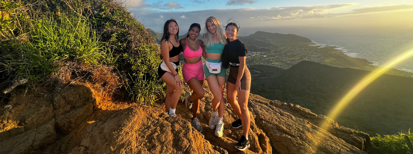 Photo shows a group of four posing on a mountain top hiking scene