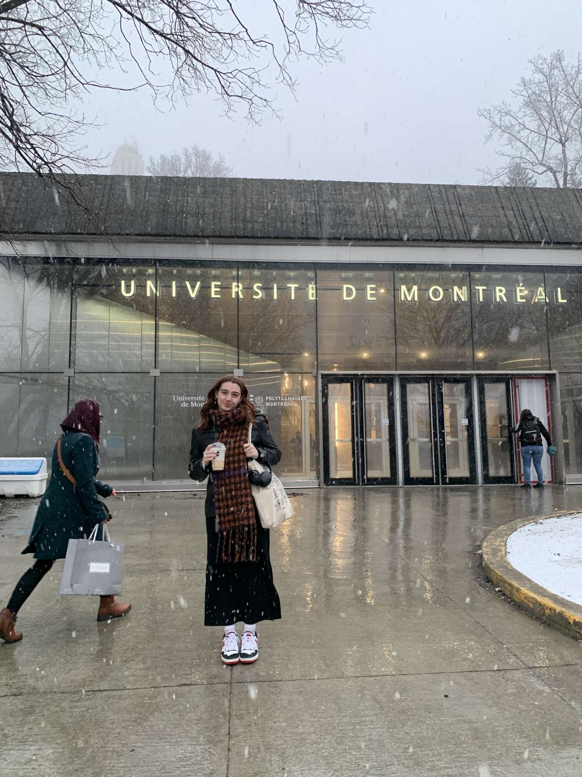 Image shows a student posing in a snow falling scene, in front of a modern building