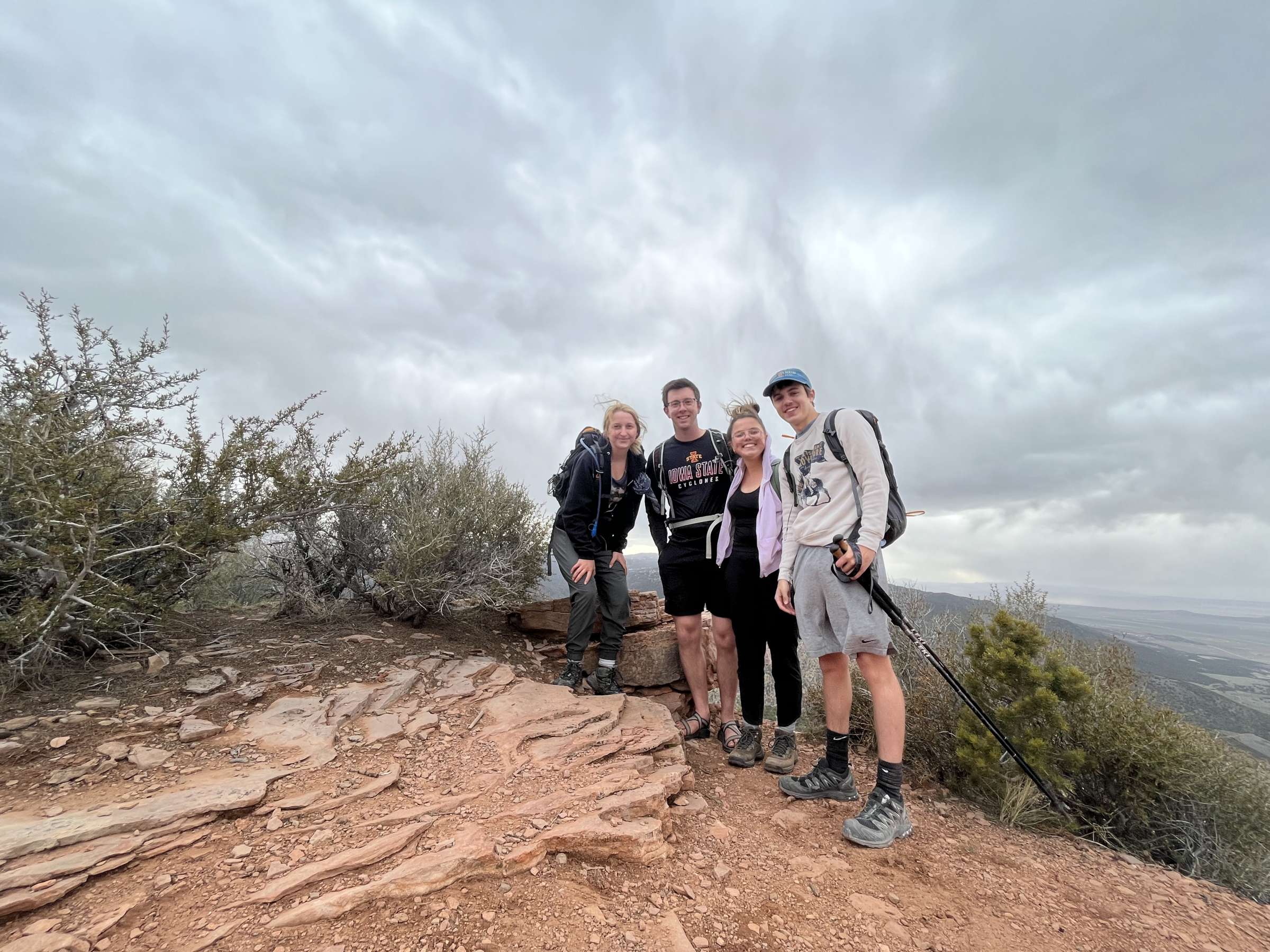 Image shows a group posing on a hike against a cloudy background